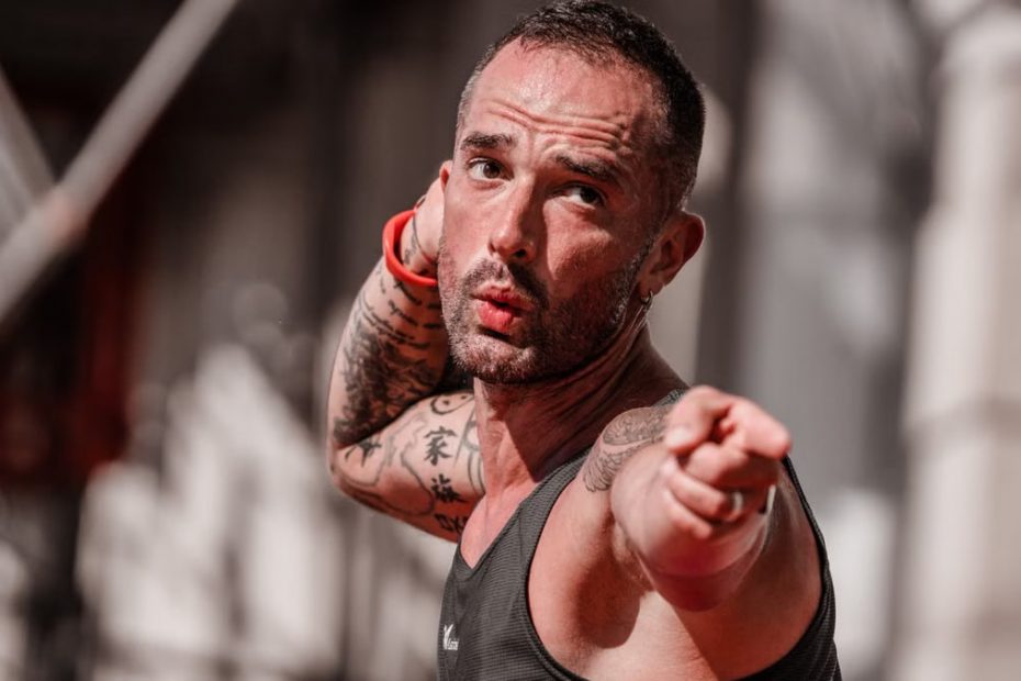 Tattooed man in a tank top points with focus during outdoor fitness activity in A Coruña.